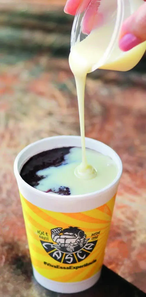 Leite condensado sendo servido sobre açaí em copo oficial do Casca Açaí.