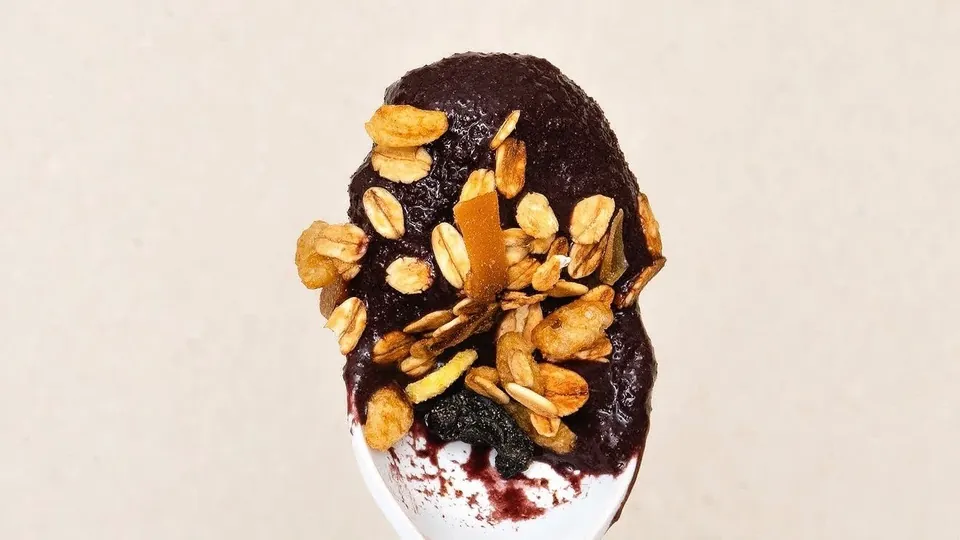 Colher com açaí cremoso coberto de granola.