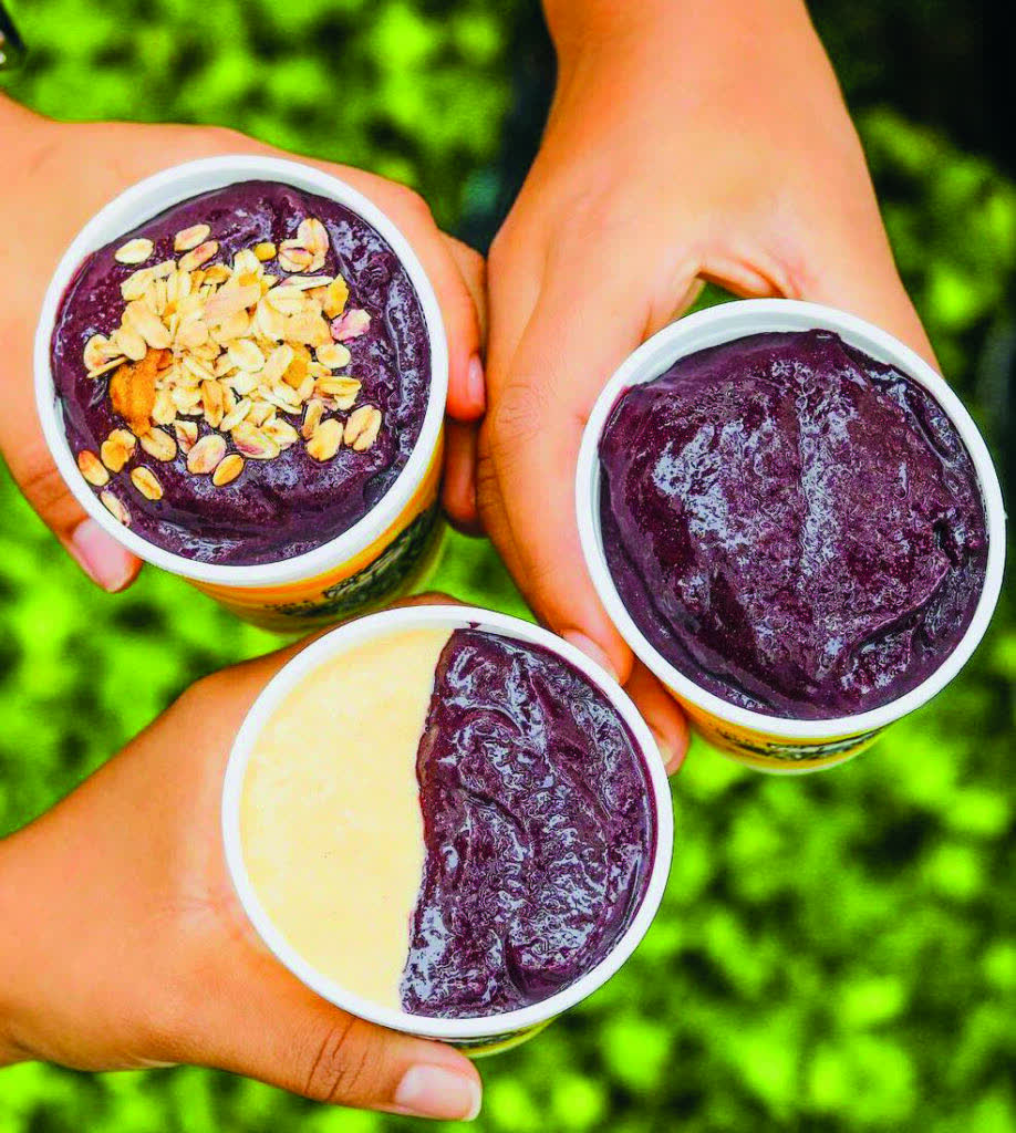 Três copos oficiais do Casca Açaí segurados ao ar livre.