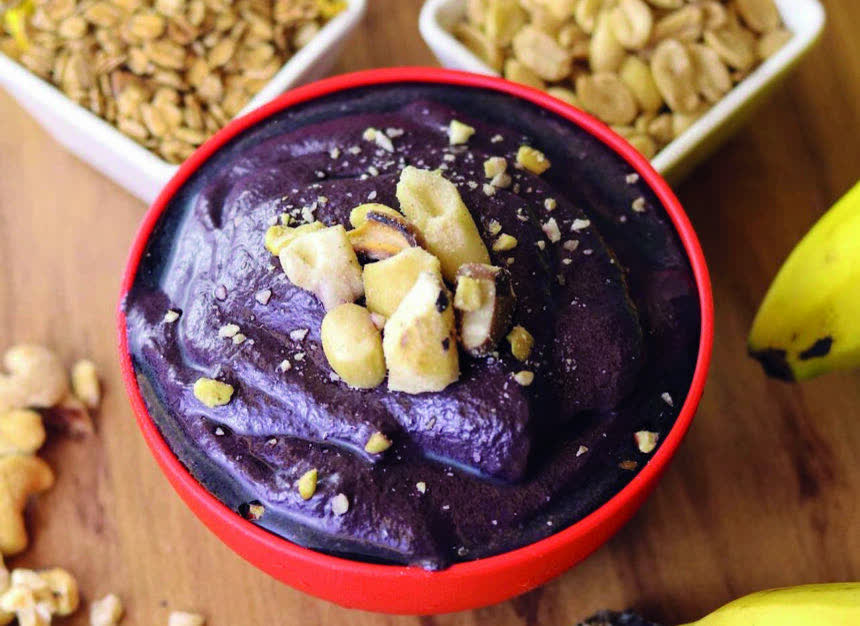 Açaí em tigela com castanhas, granola e banana ao lado.